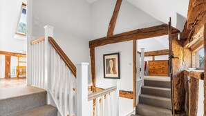 Eine Treppe mit weißen Geländern und Holzträgern, die zu einem Raum führt, in dem sich ein Heizkörper und ein gerahmtes Bild befinden.