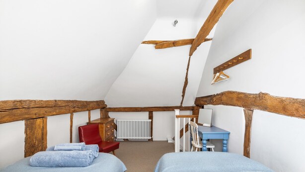 Ein Zimmer mit zwei Betten, einem roten Sessel, einem Holztisch und einer Heizung.