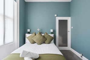 A bedroom with a bed, pillows, a nightstand, a lamp, and a door. - Seaside Haven | By My Getaways (Brighton)