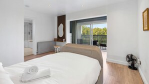 A modern bedroom with a large bed, a small bedside table, a radiator, and a view of the outdoors through a sliding glass door.