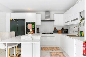 A modern kitchen with white cabinetry, a central island, and a built-in stove. - Downs Heights | By My Getaways (Brighton)