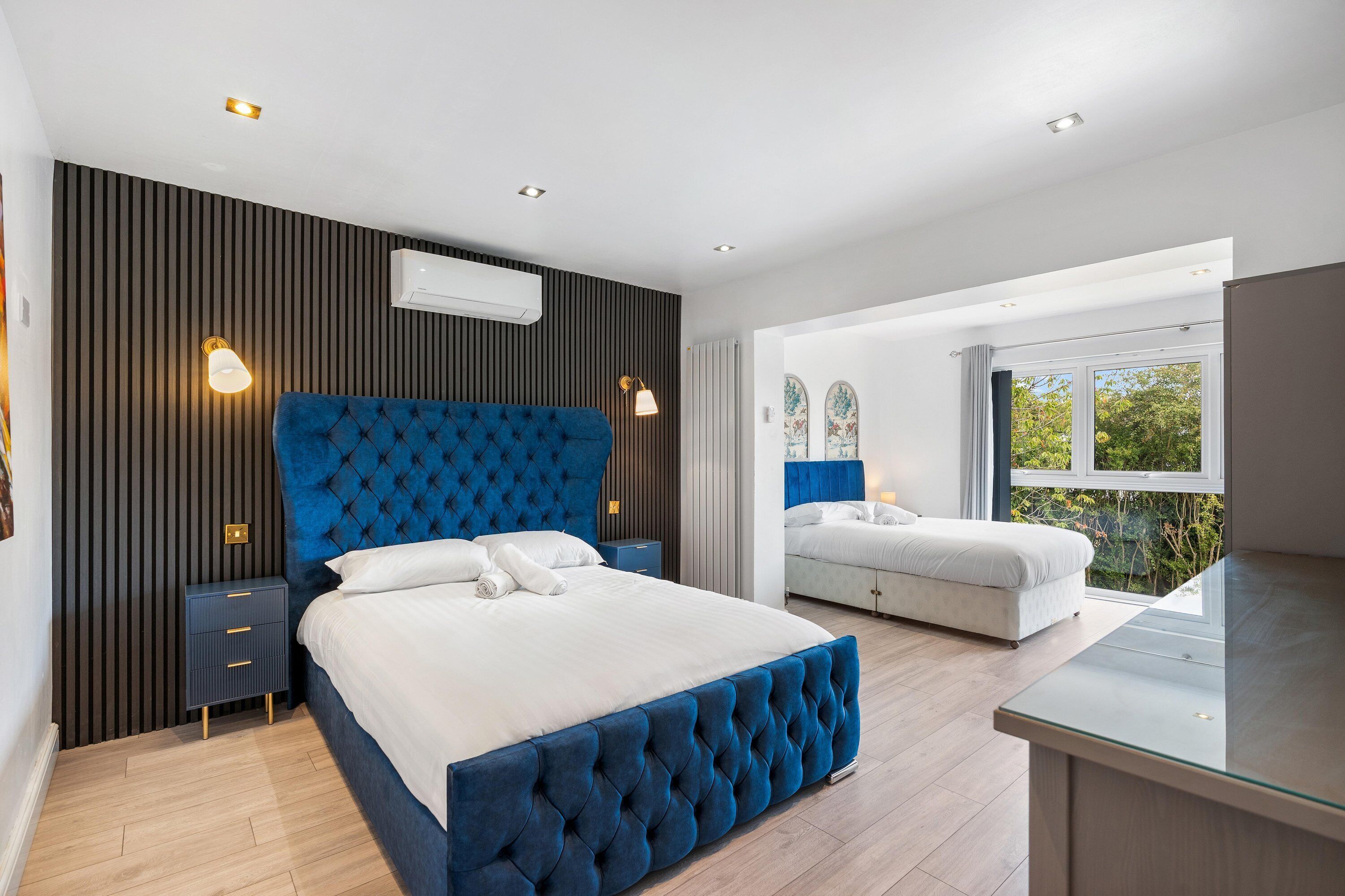 Quarto moderno com uma cama grande, uma cama menor, uma escrivaninha e vista para o verde lá fora.