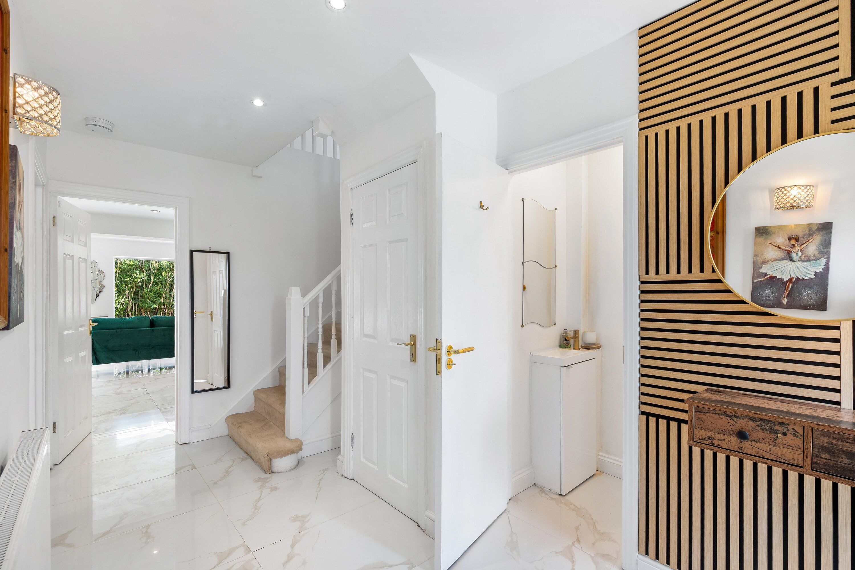 A hallway with a staircase leading to a room, a door with a mirror, and a wall with a wooden panel and a picture.