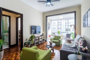 A modern living room with a herringbone floor, green sofas, a coffee table, and a flat-screen TV mounted on the wall. - 3 Quartos a 100m da Praia com AC  (Rio de Janeiro)