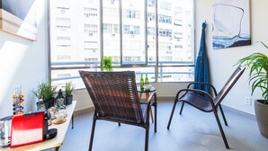 A balcony with wicker chairs, a small table with bottles, and a red appliance. - 3 Quartos a 100m da Praia com AC  (Rio de Janeiro)