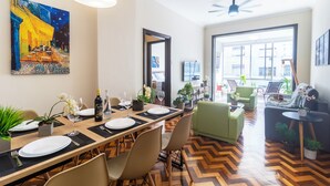 A dining area with a long table set for a meal, chairs, a ceiling fan, and a large window with a view of the outside. - 3 Quartos a 100m da Praia com AC  (Rio de Janeiro)
