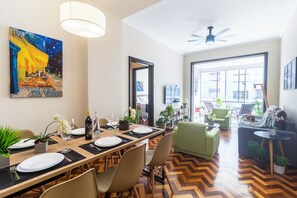 Ein Essbereich mit einem langen Tisch, der für eine Mahlzeit gedeckt ist, Stühle, einem Deckenventilator und einem großen Fenster mit Blick nach draußen.