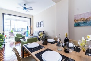Un coin repas avec une table dressée pour deux personnes, un ventilateur de plafond et une grande fenêtre.