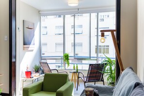 Un salon moderne avec un canapé vert, un fauteuil en osier et une petite table sur laquelle se trouvent une lampe et des objets décoratifs.