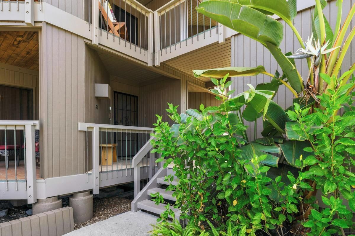 A multi-story building with balconies, a staircase, and lush greenery.
