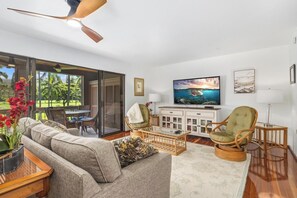 Un salon moderne avec un canapé, des fauteuils, un téléviseur et une vue sur un paysage tropical.