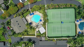 Vue aérienne d’une propriété comprenant un court de tennis, une piscine et de nombreux espaces verts.