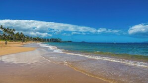 A beach with clear skies, palm trees, and a calm sea. - Maui Banyan H502 Renovated Partial Ocean View Condo Near Kamaole Beach II (Kihei)