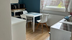 Uma cozinha compacta com mesa, cadeiras, micro-ondas e uma janela com cortinas.