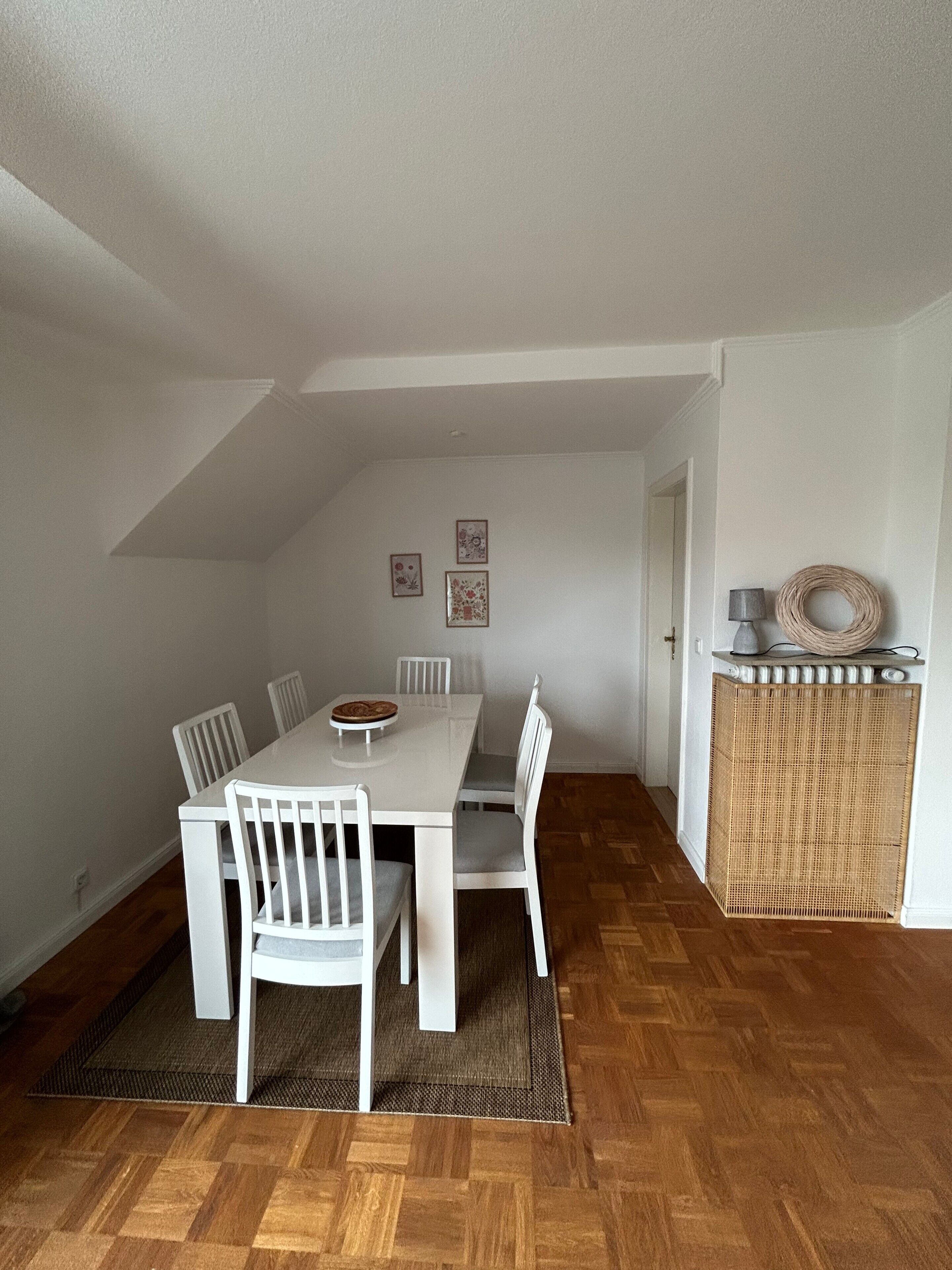 Ein Essbereich mit einem weißen Tisch und Stühlen, einem gewebten Korb auf einem Schrank und gerahmten Bildern an der Wand.