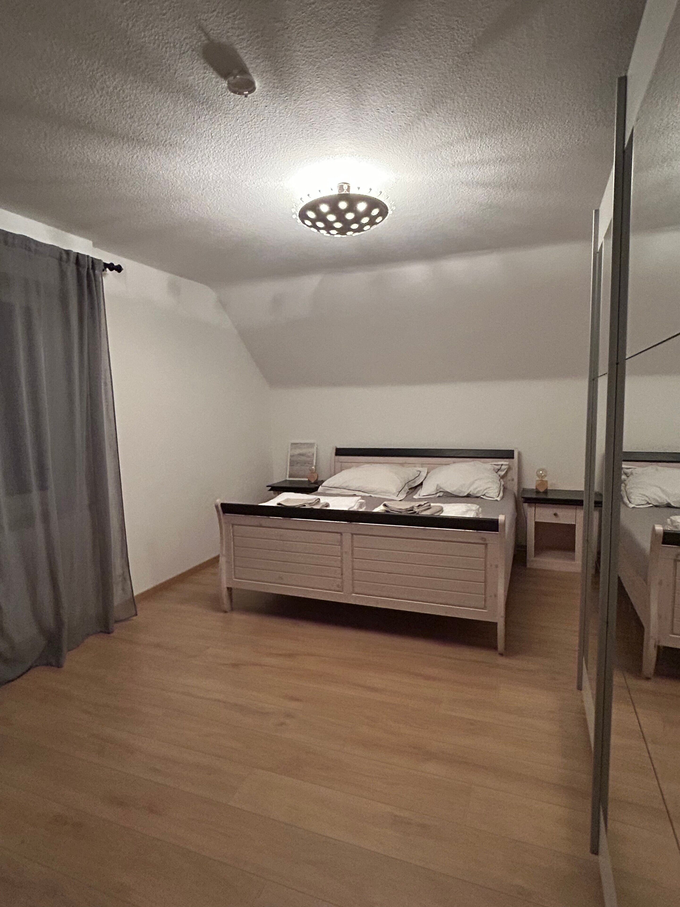 Une chambre à coucher avec un lit simple, une table de chevet, une commode, un miroir et un luminaire au plafond.