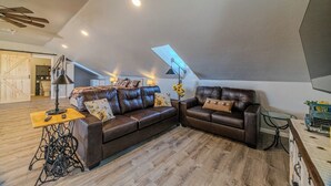 A loft-style living room with a brown leather sectional sofa, a small wooden table, and a ceiling fan.