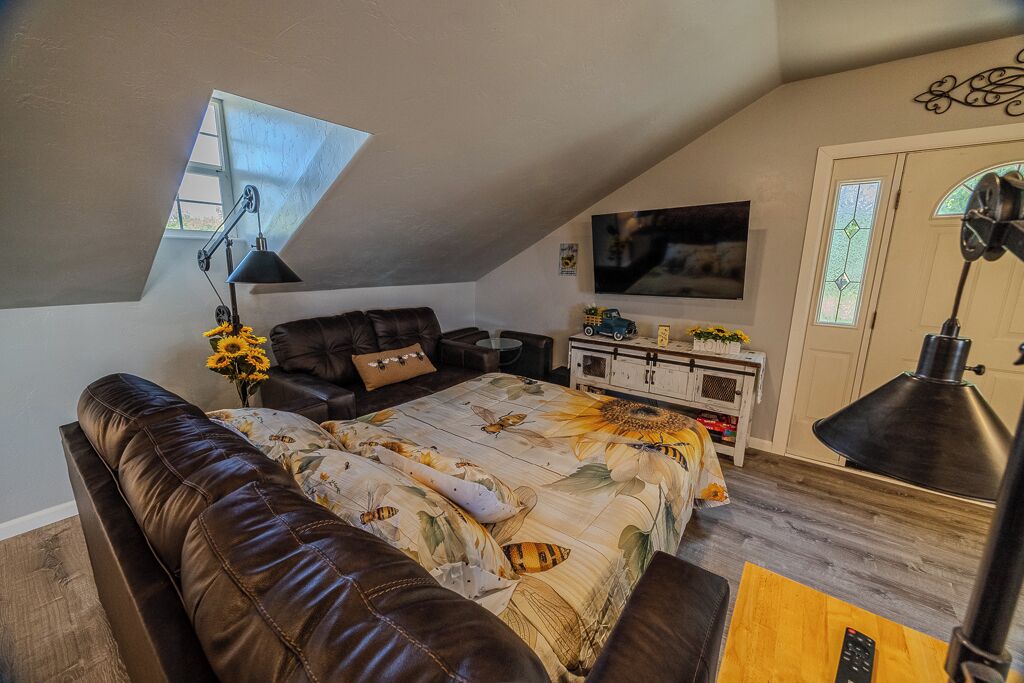 A loft bedroom with a sloped ceiling, a large bed, a sofa, a TV, and a desk.