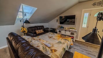 A loft bedroom with a sloped ceiling, a large bed, a sofa, a TV, and a desk.