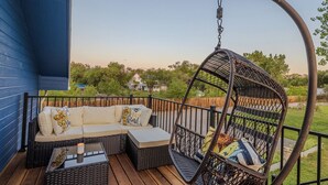 A deck with a wicker sofa and a hanging chair, overlooking a backyard.