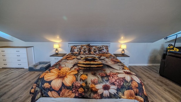 A bedroom with a floral bedspread, two bedside lamps, a dresser, and a small table with a decorative item.