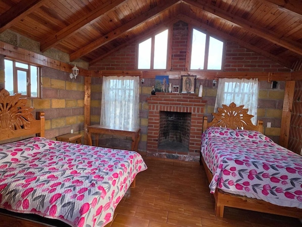 A cozy room with two wooden beds, a brick fireplace, and a wooden ceiling.