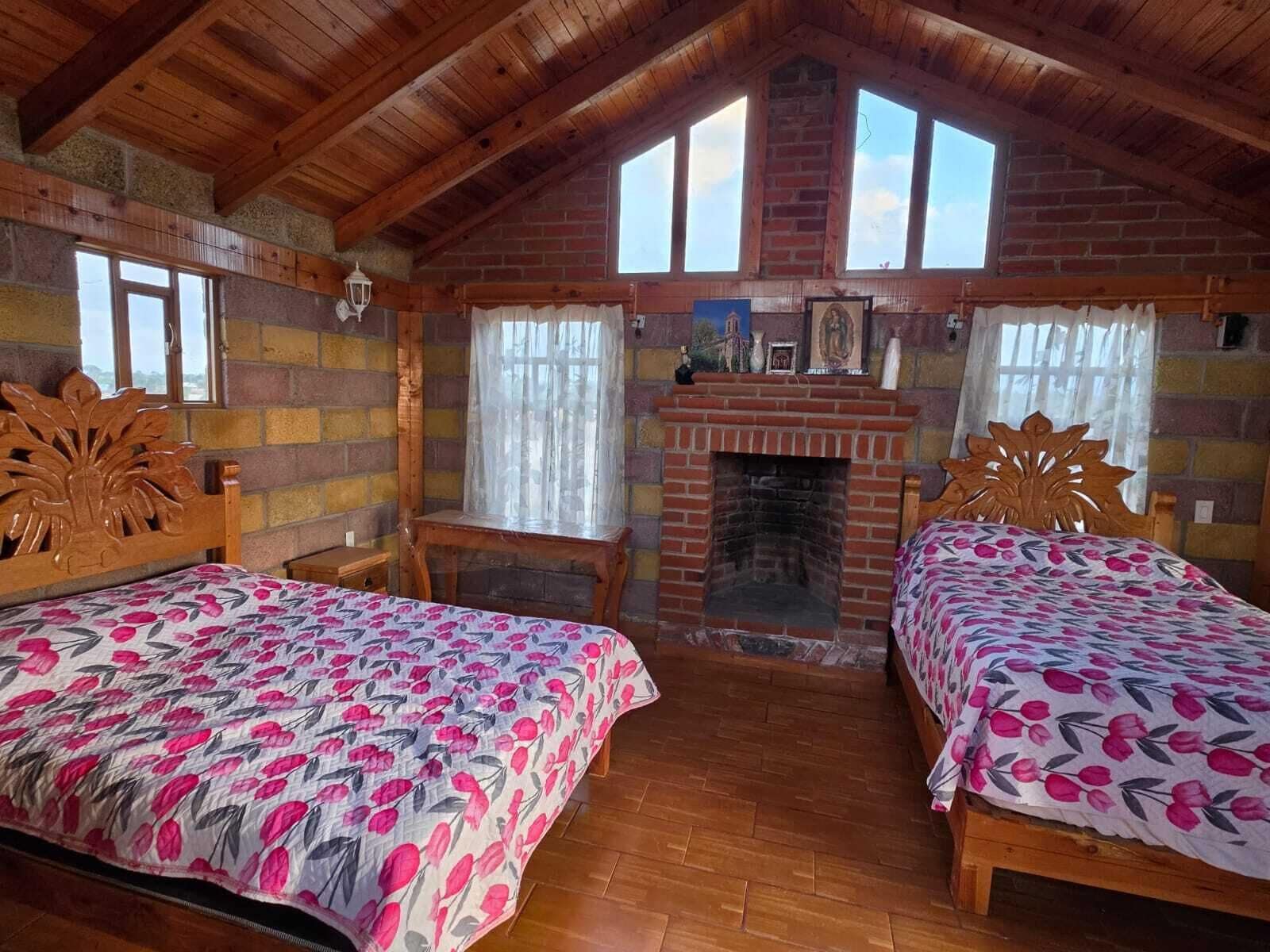Una habitación acogedora con dos camas de madera, una chimenea de ladrillo y una ventana con cortinas.