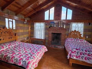 Una habitación acogedora con dos camas de madera, una chimenea de ladrillo y una ventana con cortinas.