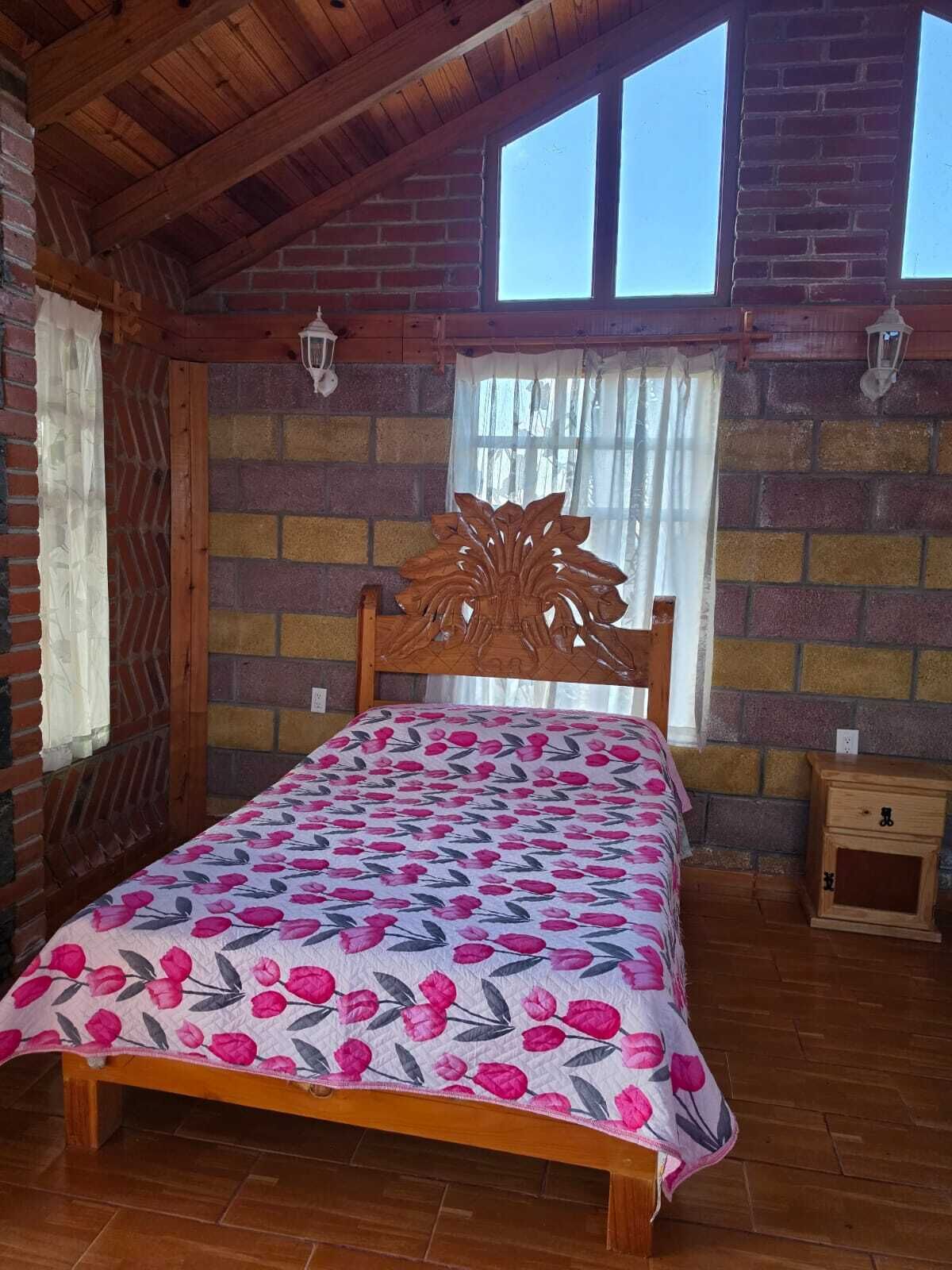 Un dormitorio con cama de madera, pared de ladrillo y ventana con cortinas.