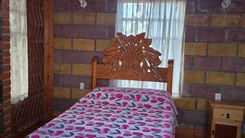Un dormitorio con cama de madera, pared de ladrillo y ventana con cortinas.