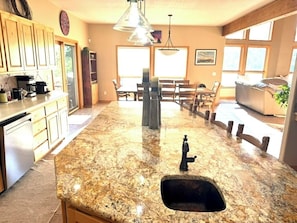 A kitchen with granite countertops, a sink, and wooden cabinets. There is a dining area with a table and chairs visible in the background. - Sunrise Ridge|Great Views,Hot Tub, +Pets, 10 Acres (Angel Fire)