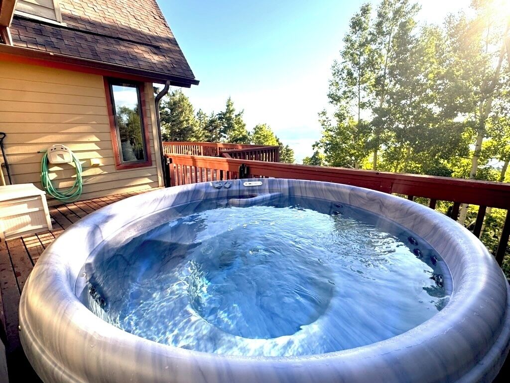 An outdoor hot tub on a wooden deck with a house in the background.