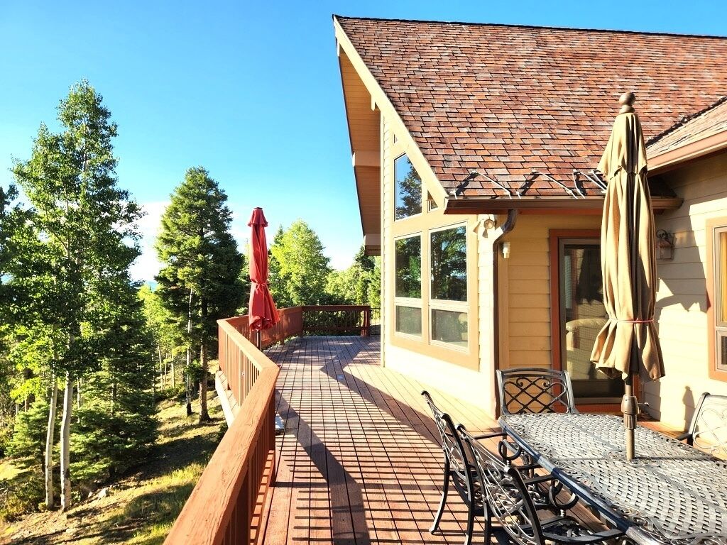 A wooden deck with outdoor furniture, a red umbrella, and a building with a tiled roof.