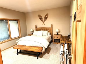 A bedroom with a wooden bed, bedside tables, a bench, a window, and a wall-mounted decoration. - Sunrise Ridge|Great Views,Hot Tub, +Pets, 10 Acres (Angel Fire)