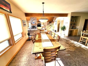 A dining area with a long wooden table and chairs, a hanging light fixture, and a staircase leading to an upper level. - Sunrise Ridge|Great Views,Hot Tub, +Pets, 10 Acres (Angel Fire)