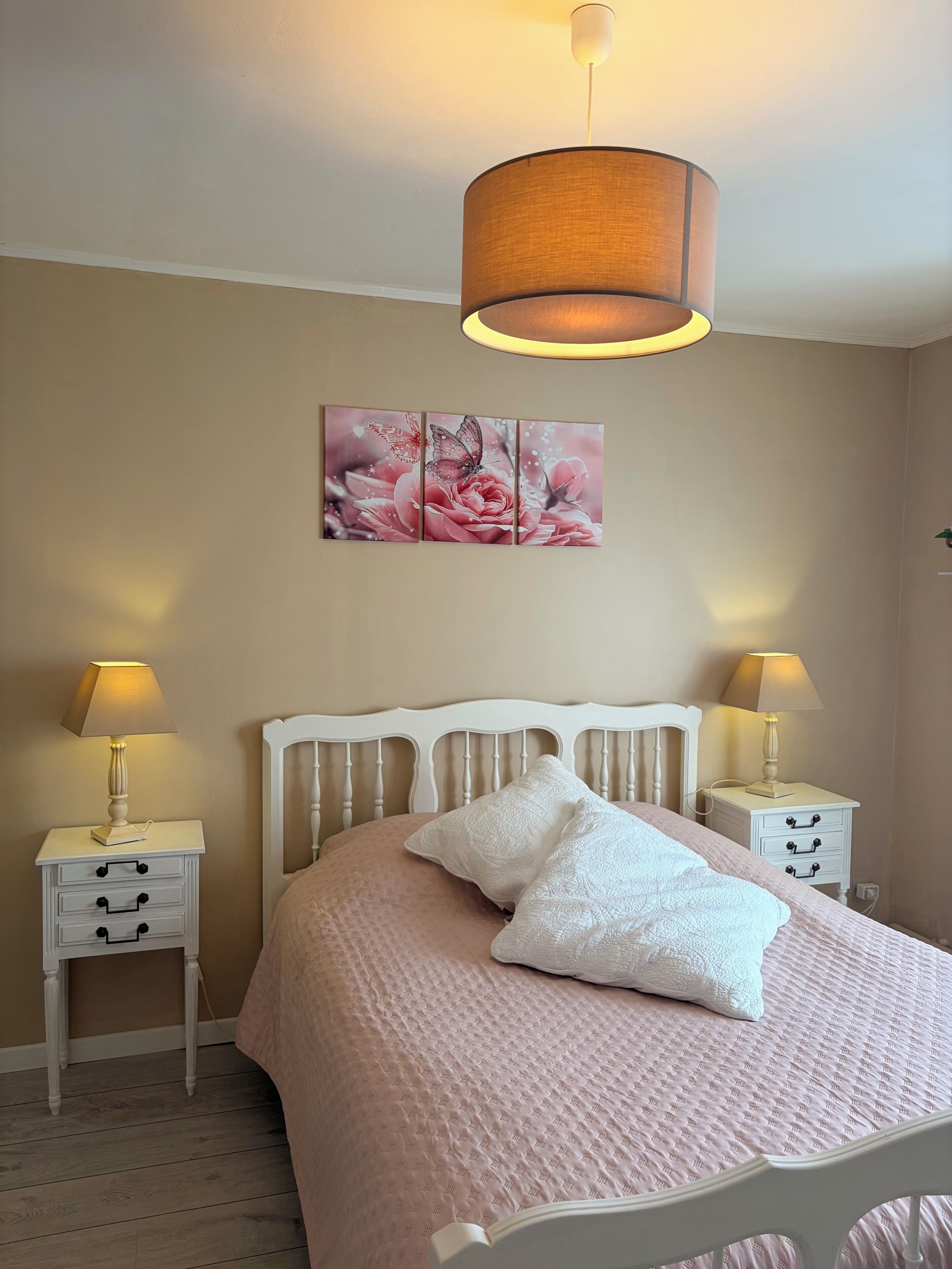 A bedroom with a bed, two bedside tables, a wall-mounted lamp, and a decorative wall piece.
