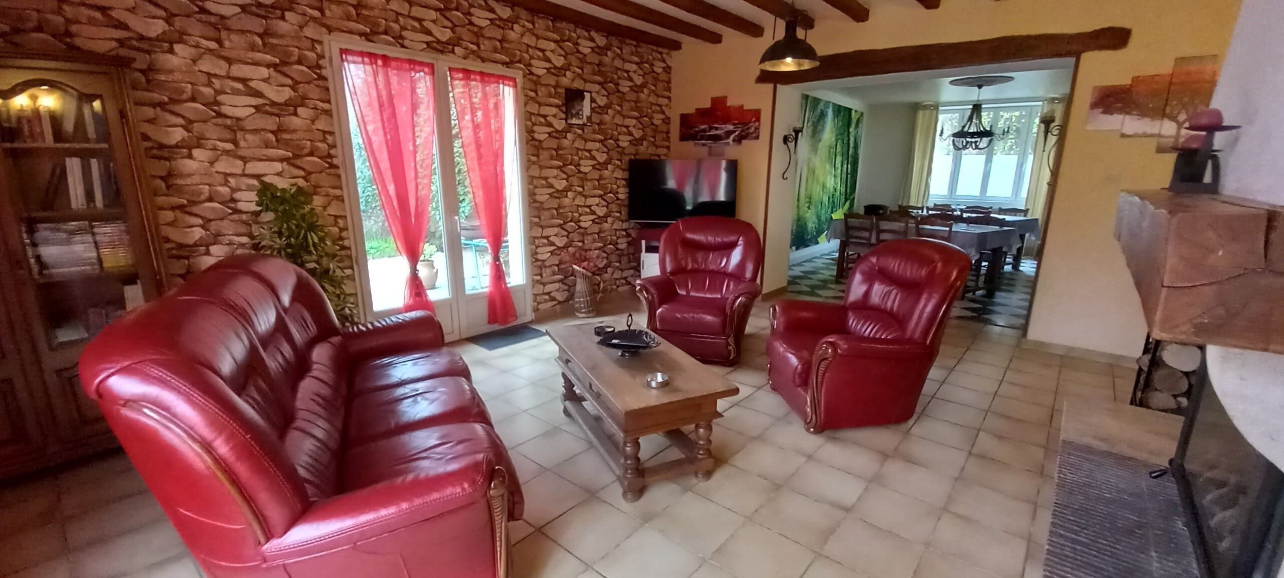 A living room with a stone wall, red leather sofas, a wooden coffee table, and a TV.