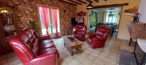 Una sala de estar con pared de piedra, sofás de cuero rojo, una mesa de centro de madera y un televisor.
