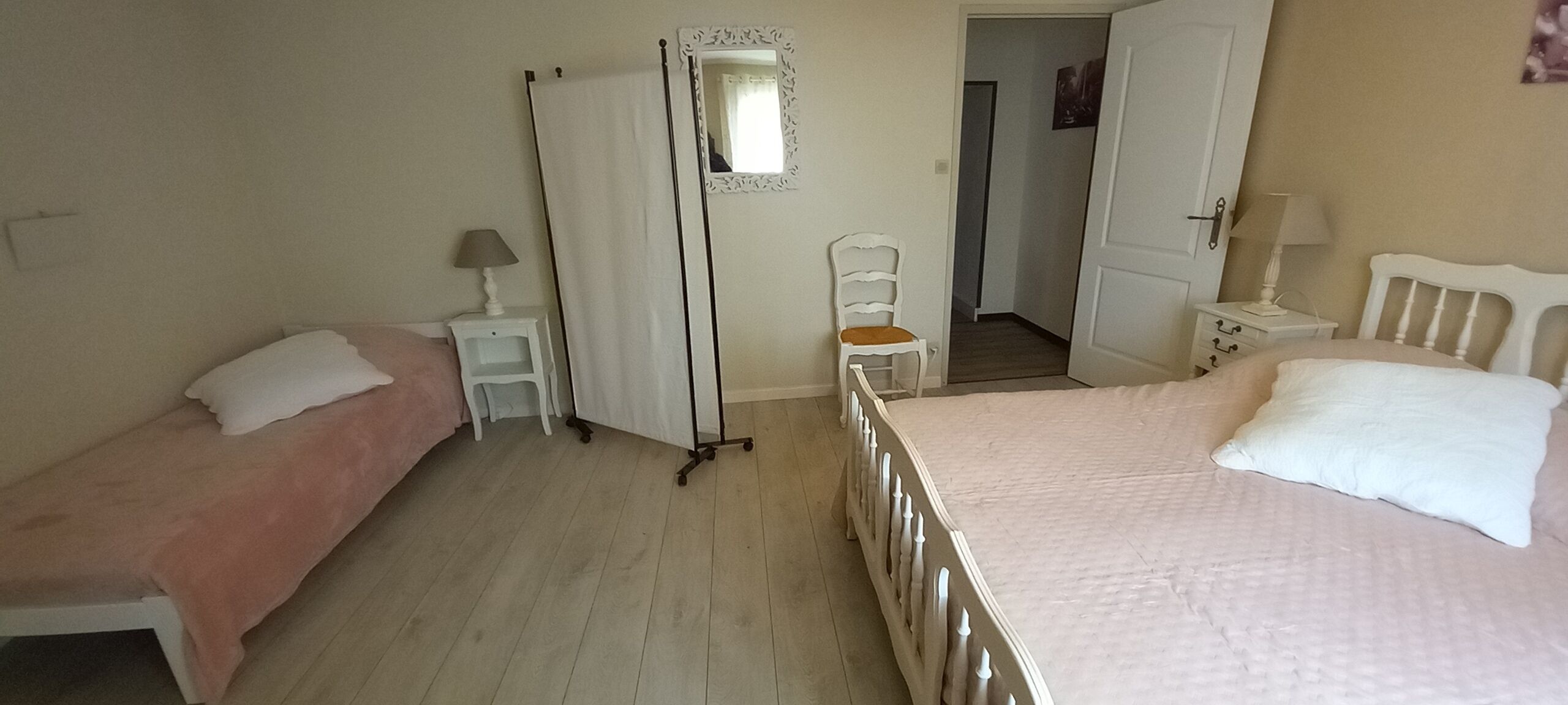 Um quarto com duas camas de solteiro, uma cadeira, um guarda-roupa e um espelho.