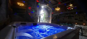Ett bubbelbad med vattenstrålar, omgivet av en stenmur och med utsikt över en byggnad genom en välvd öppning.