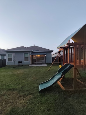 A backyard with a slide, a barbecue grill, and a picnic table. - Cozy 3BR home in the Woodlands. Perfect for families! (Tomball)