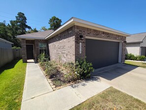 A residential house with a brick exterior, a garage, and a well-maintained lawn. - Cozy 3BR home in the Woodlands. Perfect for families! (Tomball)