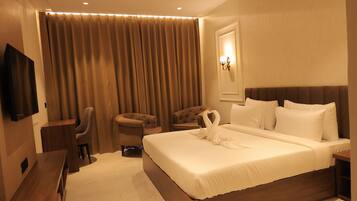 Habitación de hotel con cama, dos sillones, escritorio, televisor de pantalla plana y ventilador de techo.