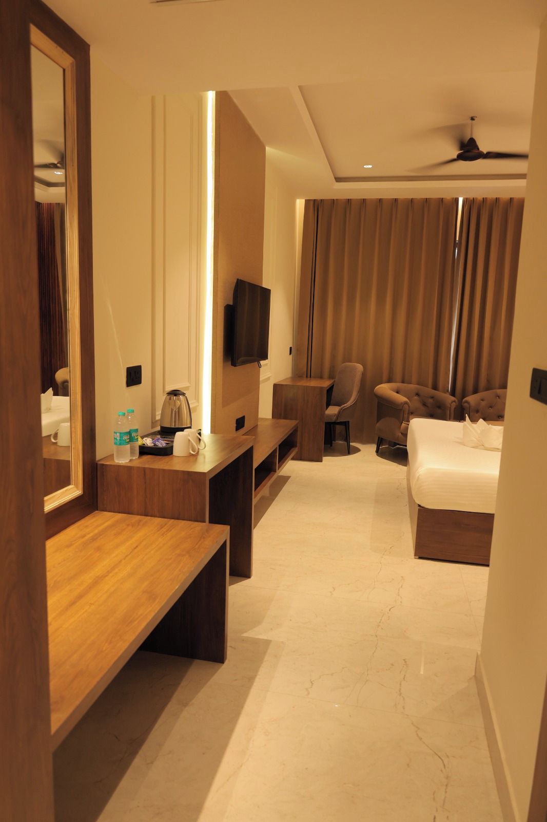 Habitación de hotel con escritorio de madera, cama, sofá, televisor y ventilador de techo.