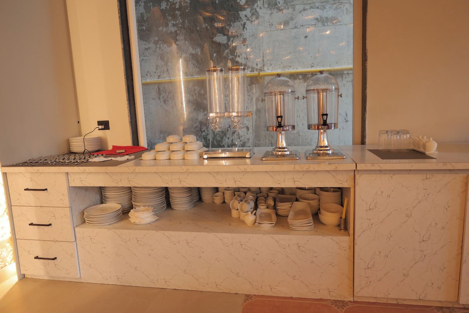 Una encimera de cocina con salpicadero de mármol, una ventana con vistas y varios utensilios de cocina.