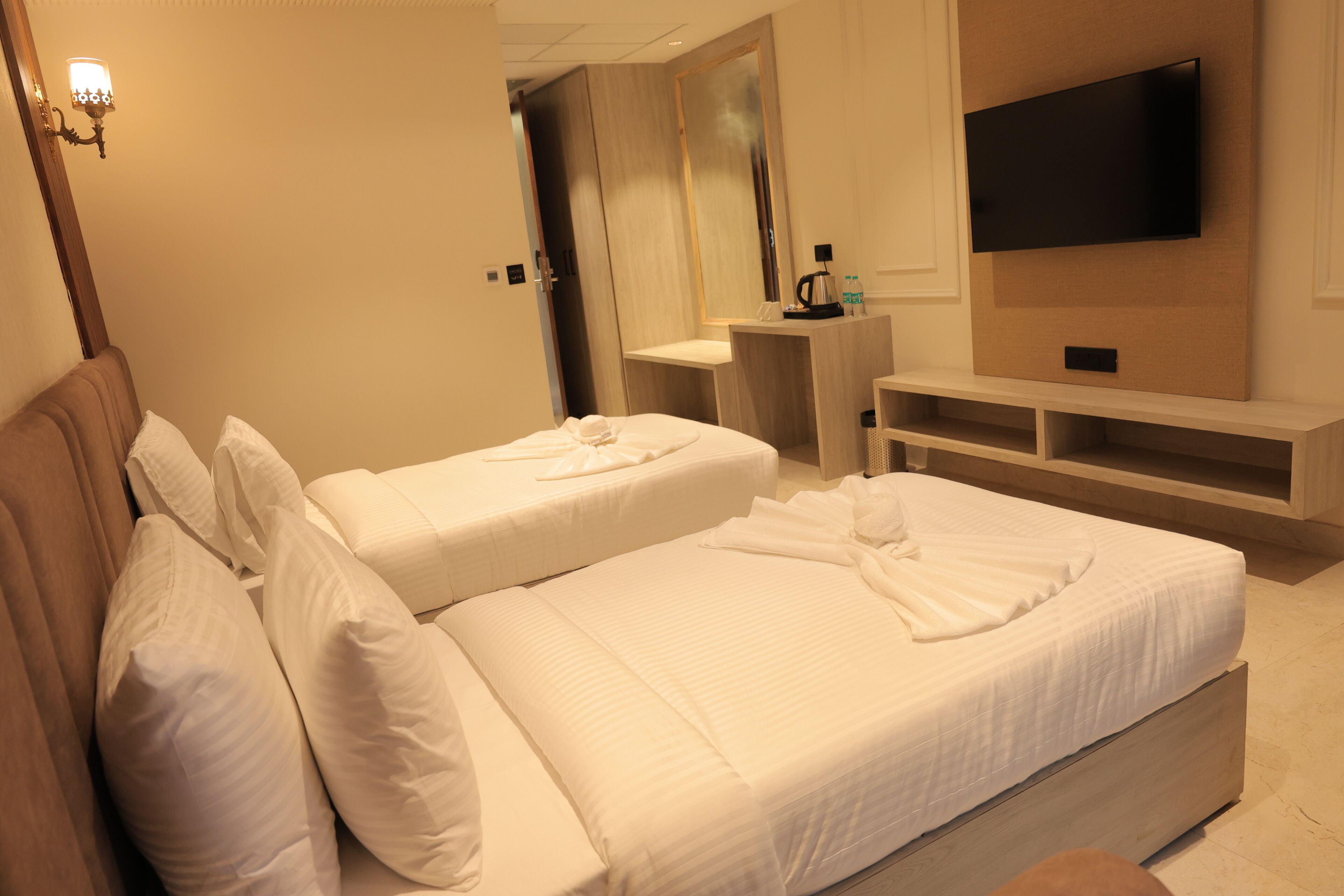 Habitación de hotel con dos camas, televisor, espejo y una pequeña mesa con tetera y botellas.