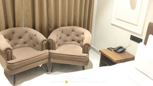 Ein Hotelzimmer mit einem Bett, zwei Sesseln, einem Nachttisch mit Telefon und einem Vorhang im Hintergrund.