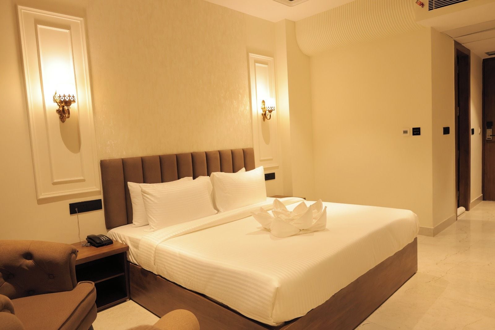 A hotel room with a large bed, bedside lamps, a nightstand, and a chair.