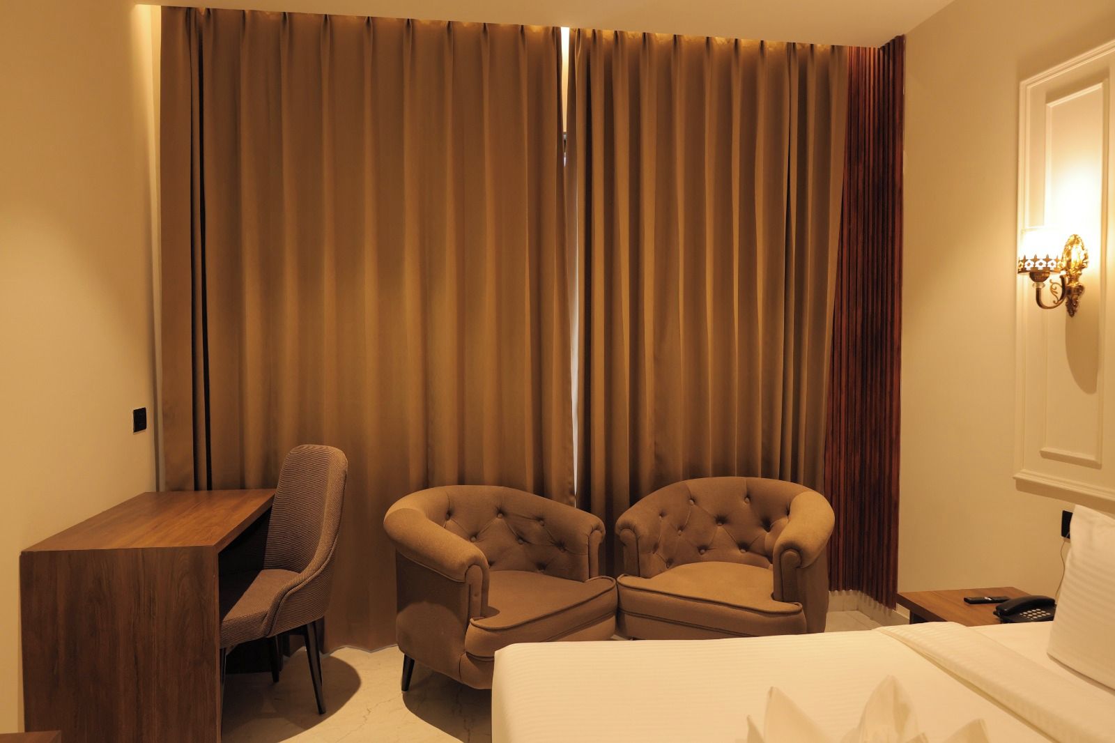 Una habitación de hotel con cama, dos sillones, un escritorio y un ventanal con cortinas.
