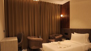 Ein Hotelzimmer mit einem Bett, zwei Sesseln, einem Schreibtisch und einem großen Fenster mit Vorhängen.